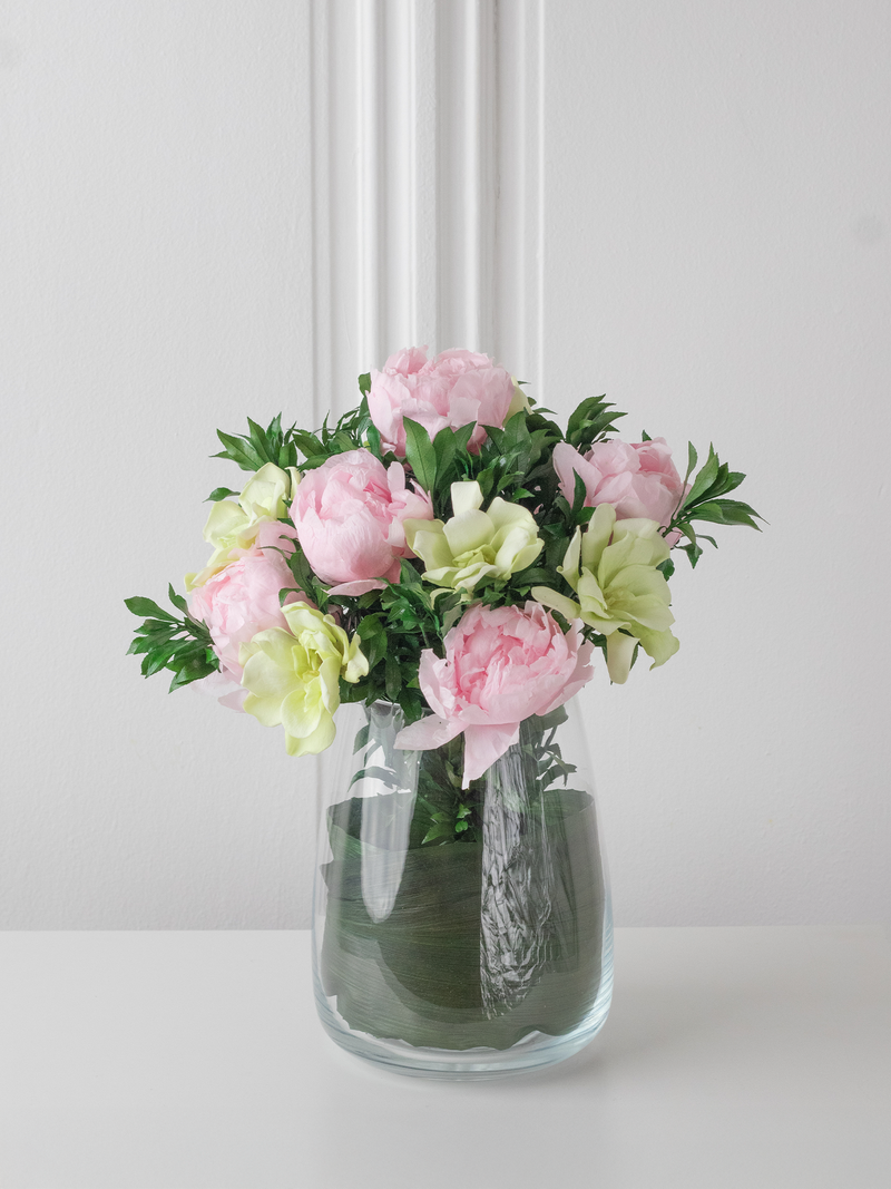 Clear glass vase with preserved pink and green flowers on a white surface. By STILLA for M/Y Vertige.