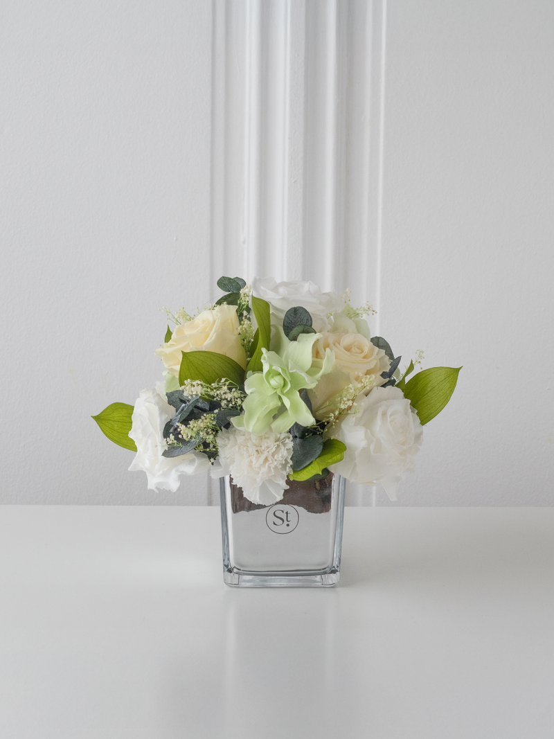 Preserved floral arrangement in a clear vase on a white surface with a light gray background. By STILLA for M/Y Vertige.