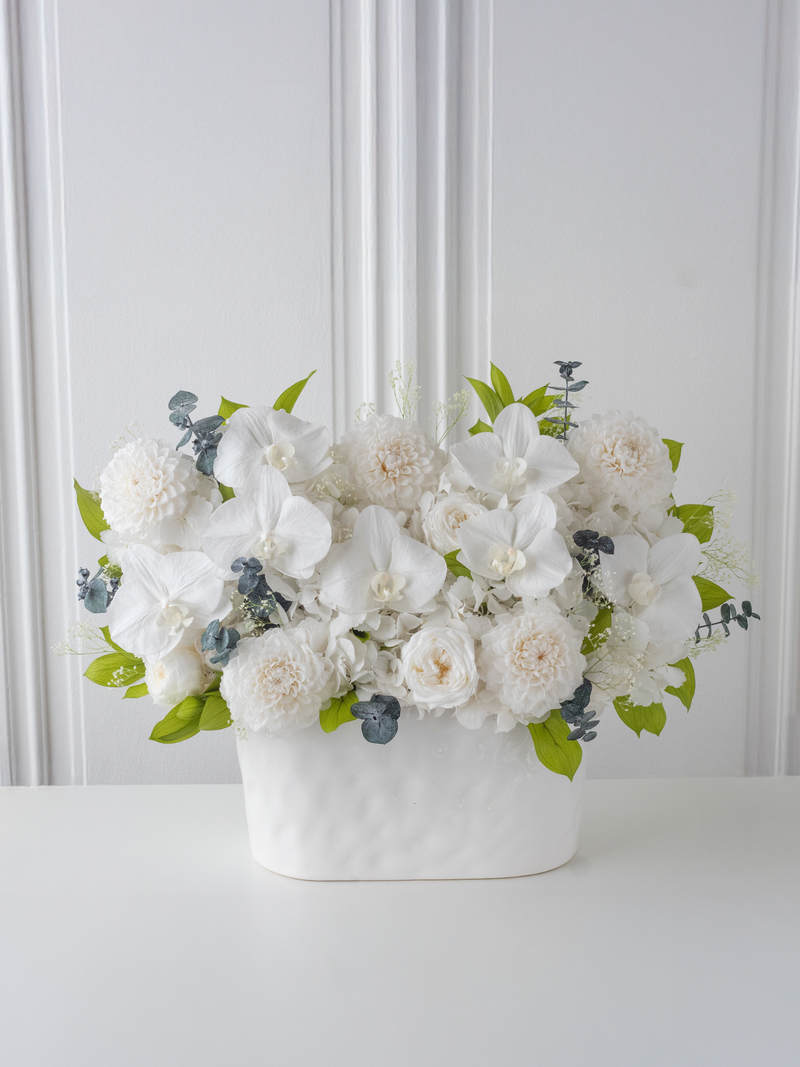 Preserved white floral arrangement in a vase against a white wall. By STILLA for M/Y Vertige.